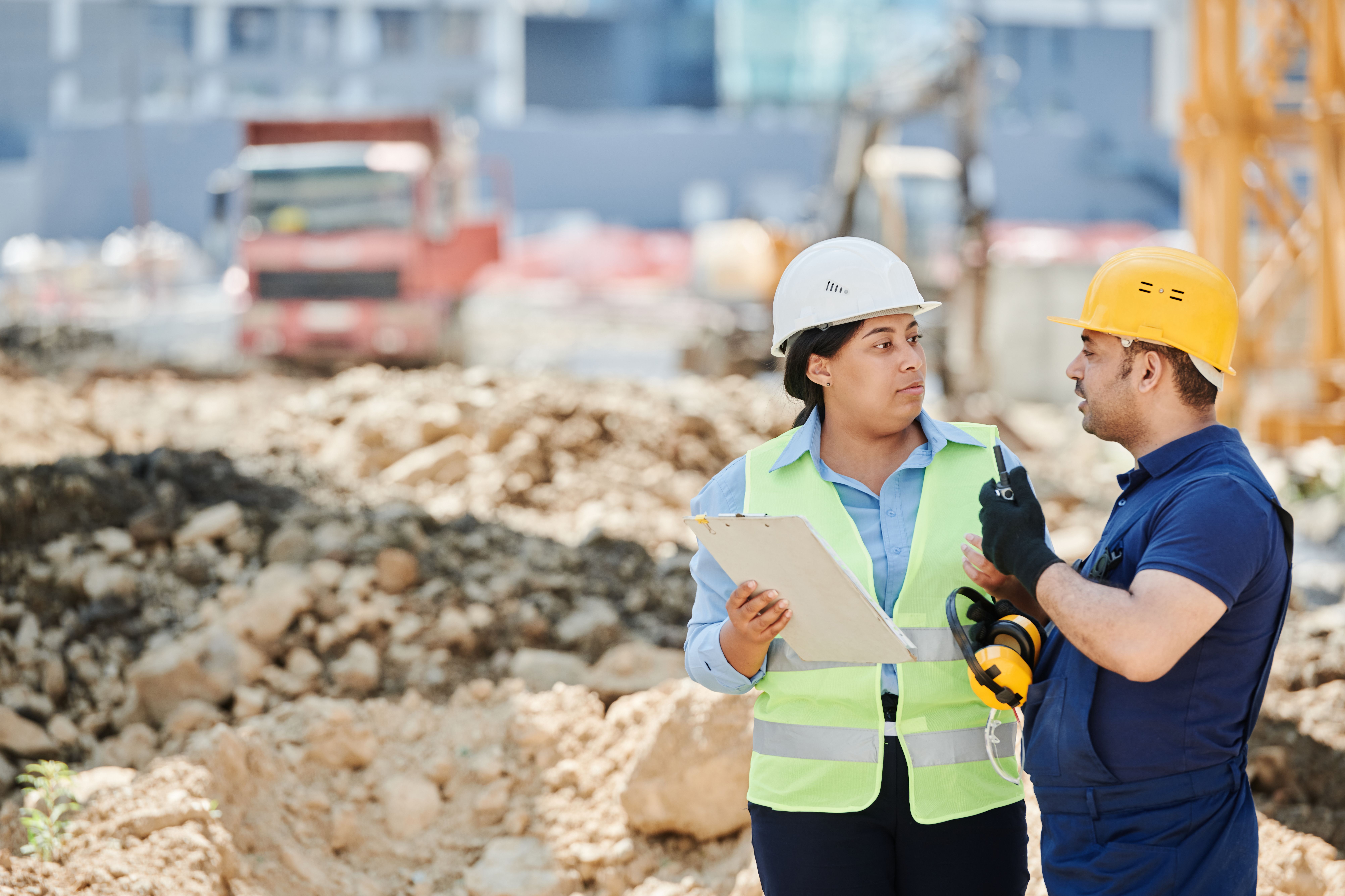 Two construction workers in hard hats and safety vests talking together at a construction site