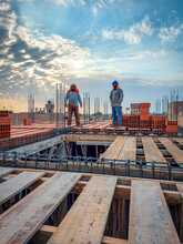 Two construction workers wearing white hard hats standing on a job site under a cloudy sky