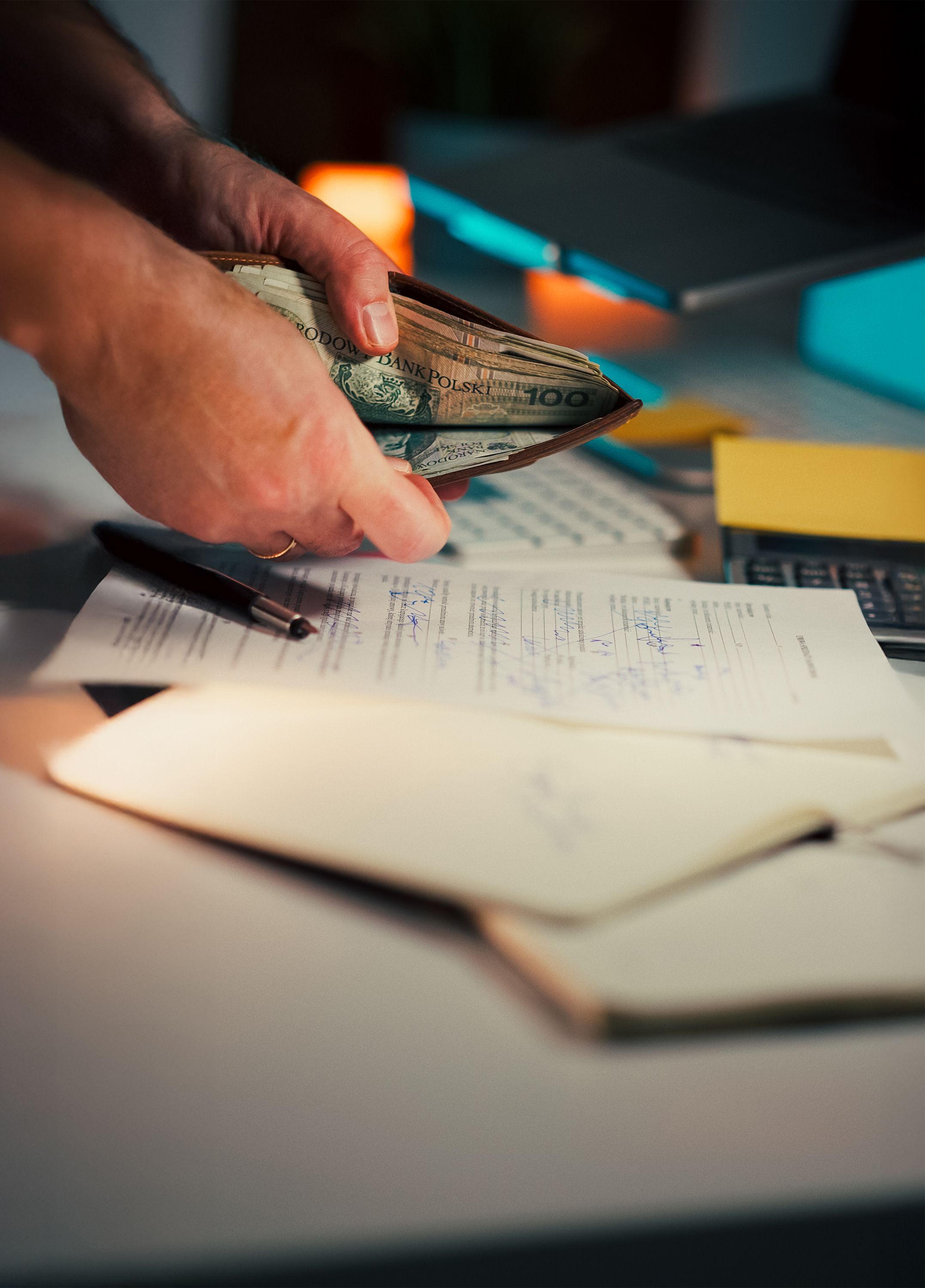 Hands counting cash banknotes next to paperwork and a pen on a desk
