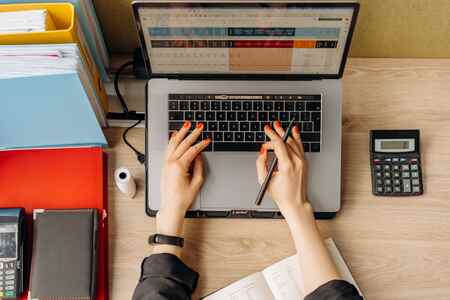 Close-up of hands typing on a laptop keyboard at an office desk with folders and a calculator