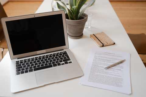 A laptop, small potted plant, and business documents laid out on a desk.
