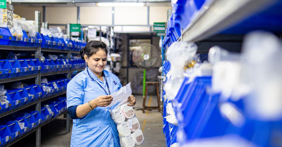A worker in a blue uniform organizing boxes and inventory on shelves in a stockroom