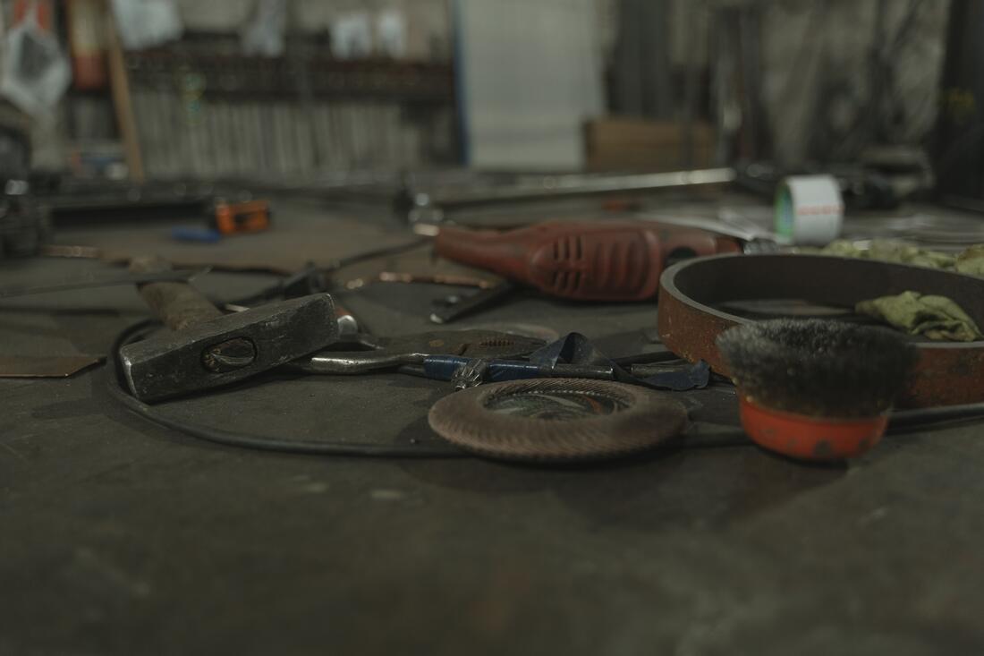 An assortment of hand tools and a power sander scattered on a metal workbench in a workshop